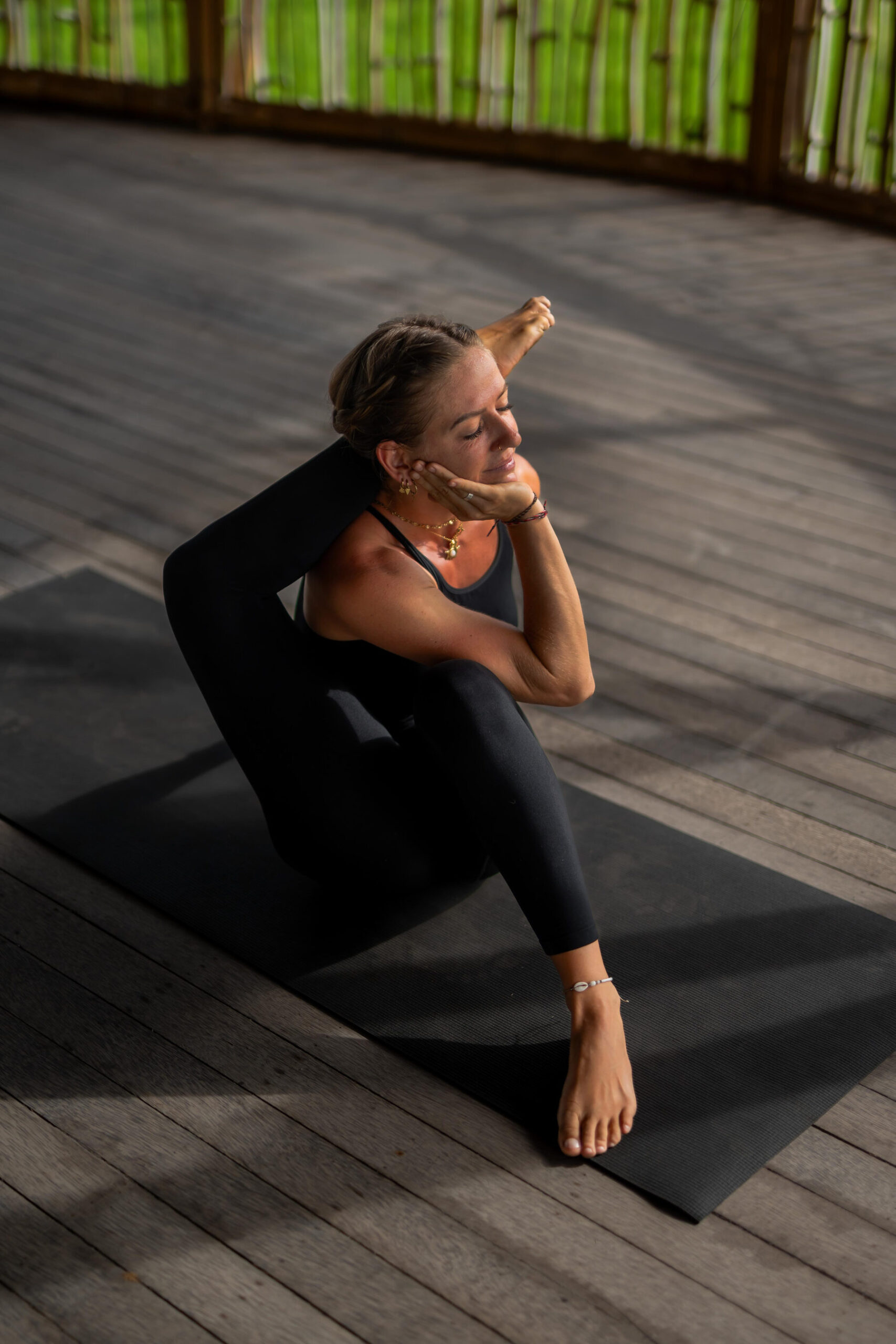 Michelle practicing eka pada sirsasana in soft sunlight on a wooden deck