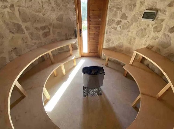 Inside the round stone sauna, curved wooden benches around the stove